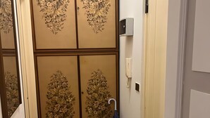 Un couloir doté d’un plancher en bois, d’une porte ornée d’un panneau décoratif à motifs floraux et d’un téléphone fixé au mur.