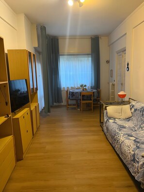 A room with a wooden floor, a sofa with a patterned cover, a television on a wooden cabinet, a dining table with chairs, and a window with curtains. - Casa Baba Apartment – Great Location in Rapallo, Ligurian Riviera (Rapallo)