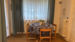 A dining area with a round table, four wooden chairs, a vase with flowers, and a window with curtains. - Casa Baba Apartment – Great Location in Rapallo, Ligurian Riviera (Rapallo)