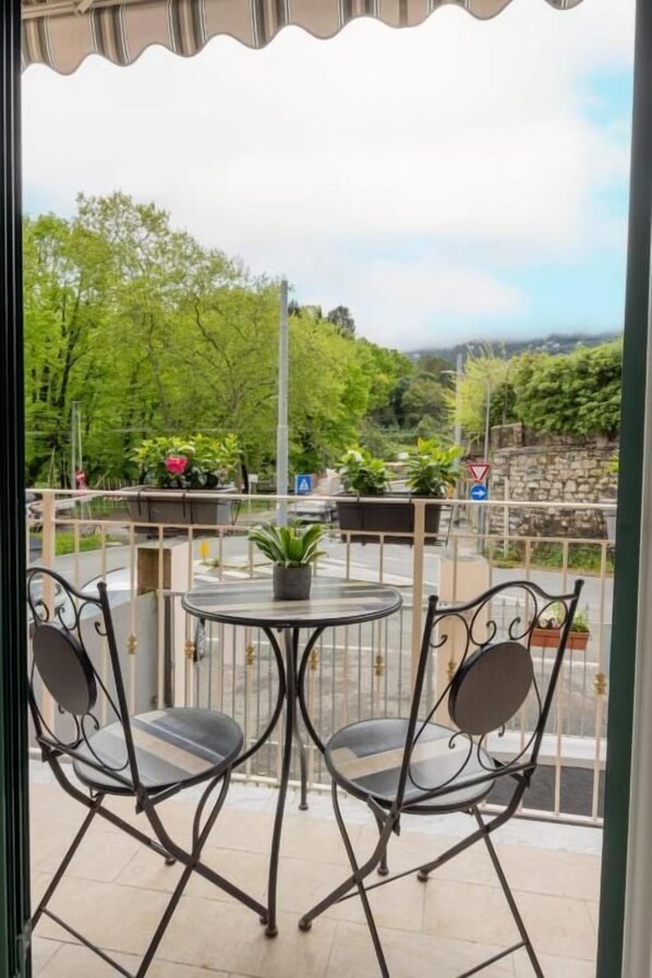 A balcony with a round table and two chairs, overlooking a garden and a stone wall.