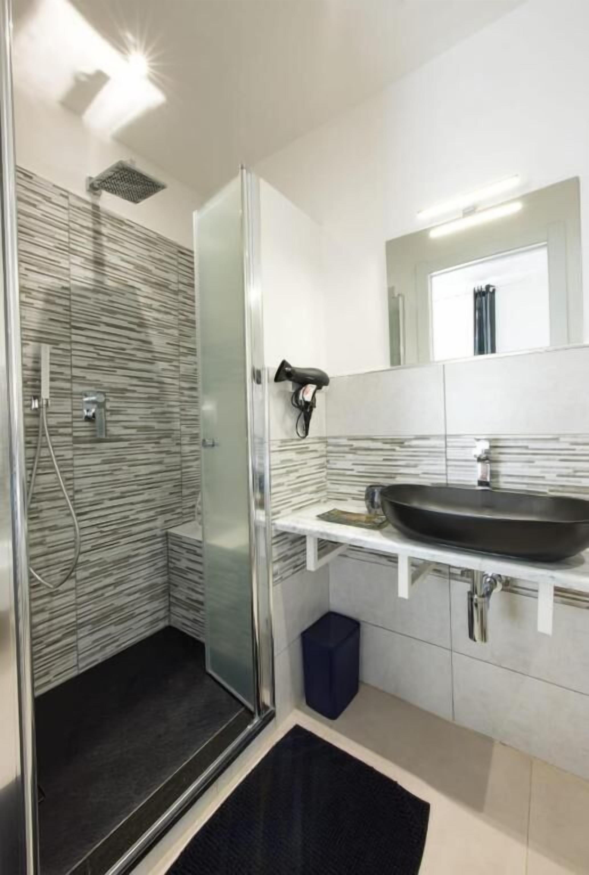 Un baño moderno con cabina de ducha de vidrio, un lavabo negro y un espejo sobre el lavabo.