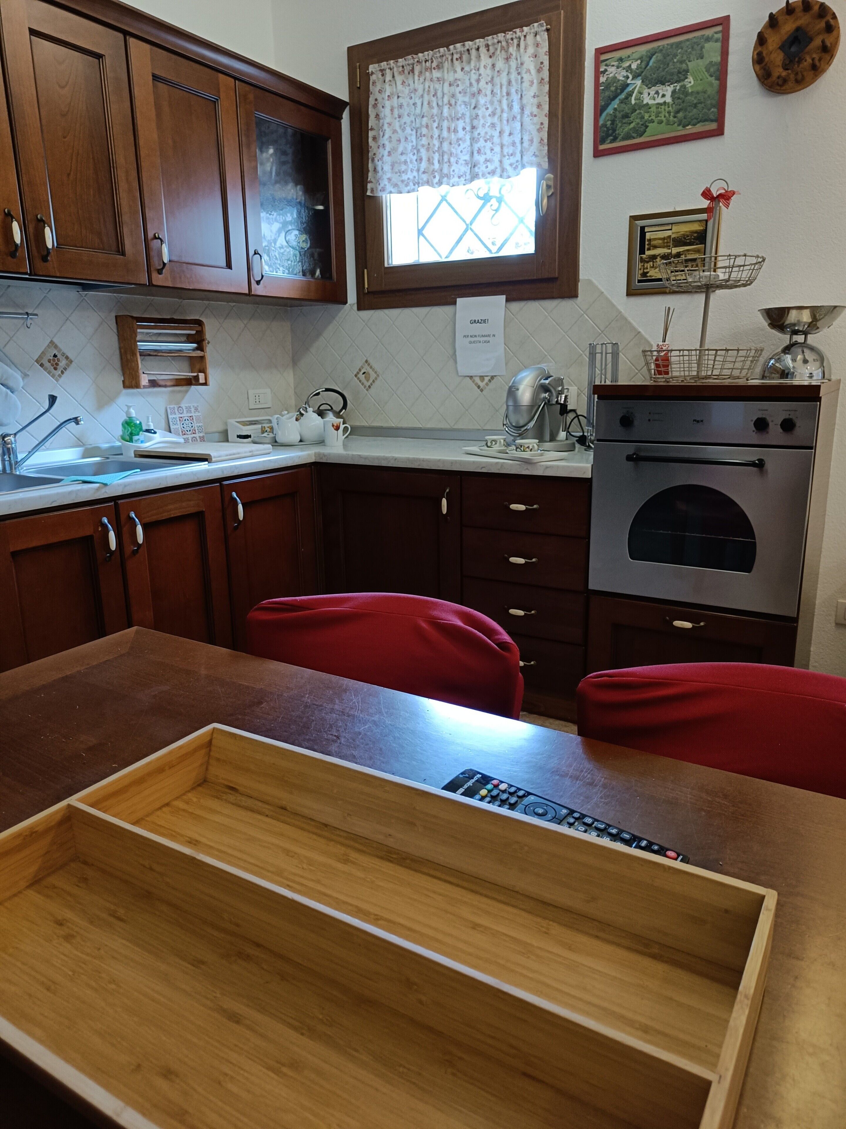 Een keuken met houten kastjes, een raam met kantgordijnen, een spoelbak en een fornuis.