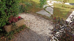 Un jardin avec un chemin de gravier, un mur de pierre et une variété de plantes.