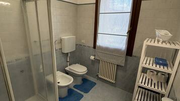 Une salle de bain comprenant une douche à parois de verre, des toilettes, un bidet, un lavabo et un porte-serviettes.