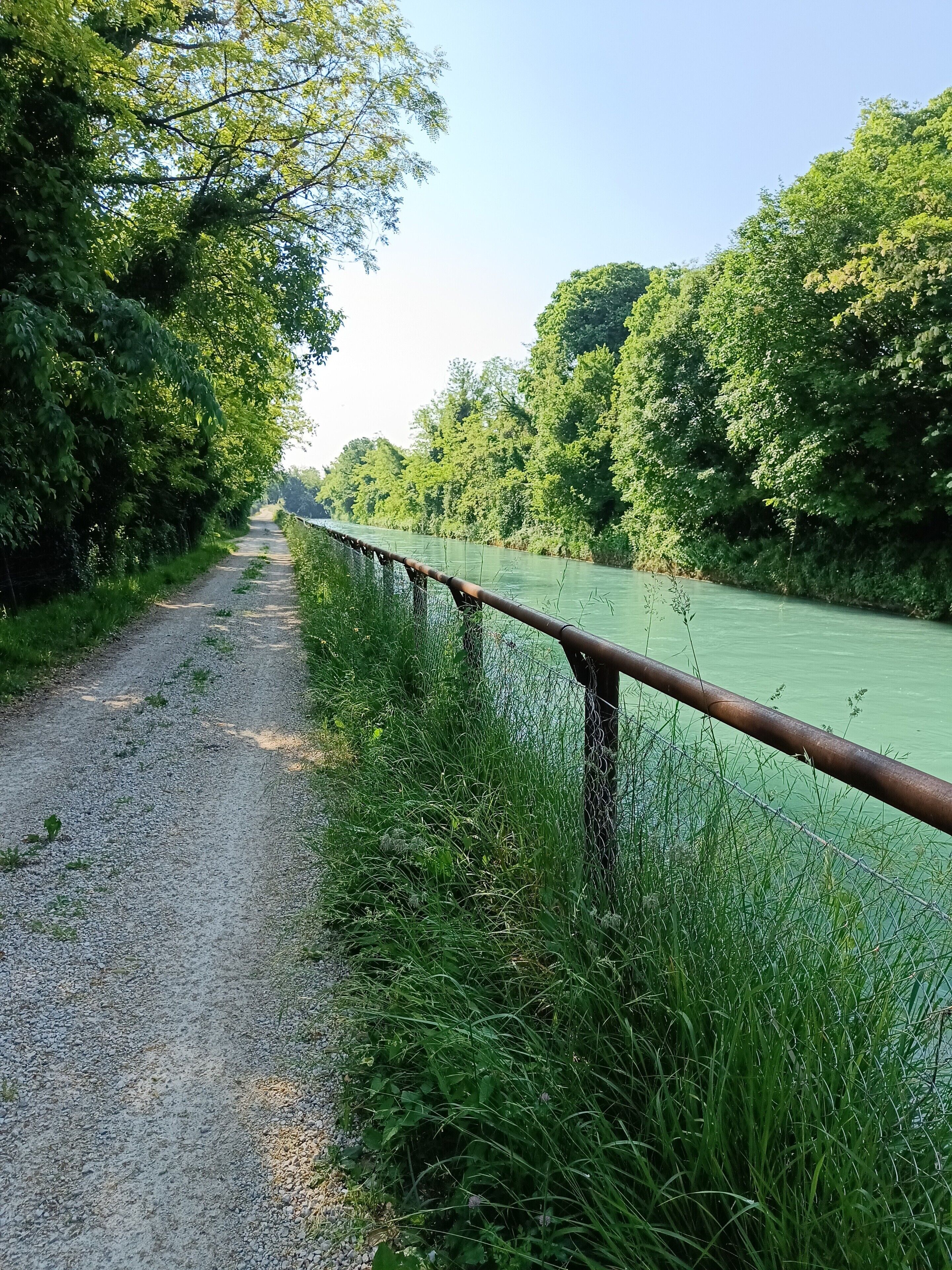 Ein Kiesweg entlang eines Flusses mit einem Metallgeländer.