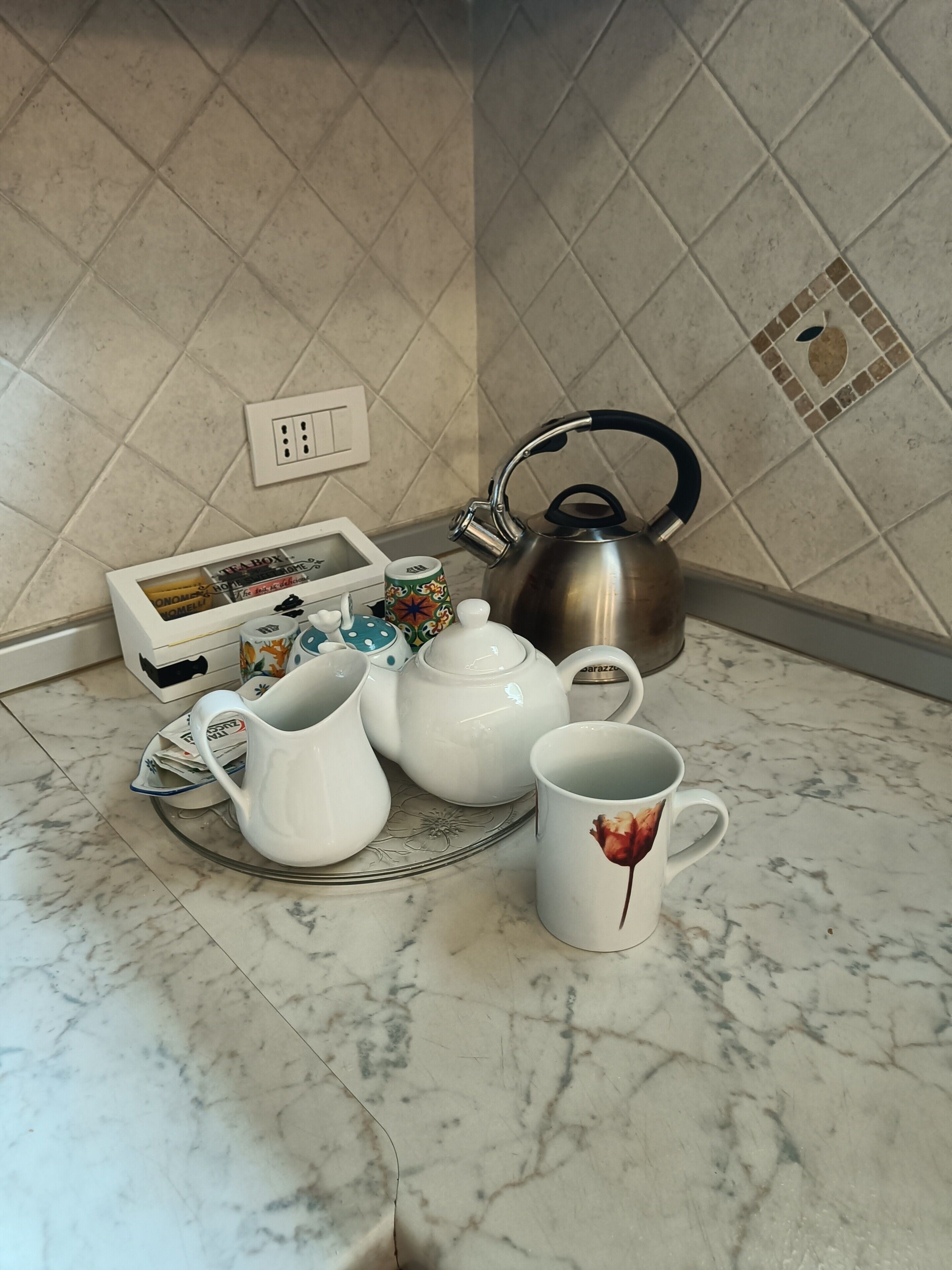 A kitchen counter with a kettle, teapot, cups, and a box of tea bags.