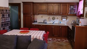 Un salon avec un canapé et une table à manger, une cuisine avec des meubles en bois et un dosseret carrelé, et un luminaire au plafond.