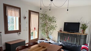 Un coin repas avec une table en bois, des chaises et un plateau. On aperçoit un canapé et un téléviseur à l’arrière-plan.