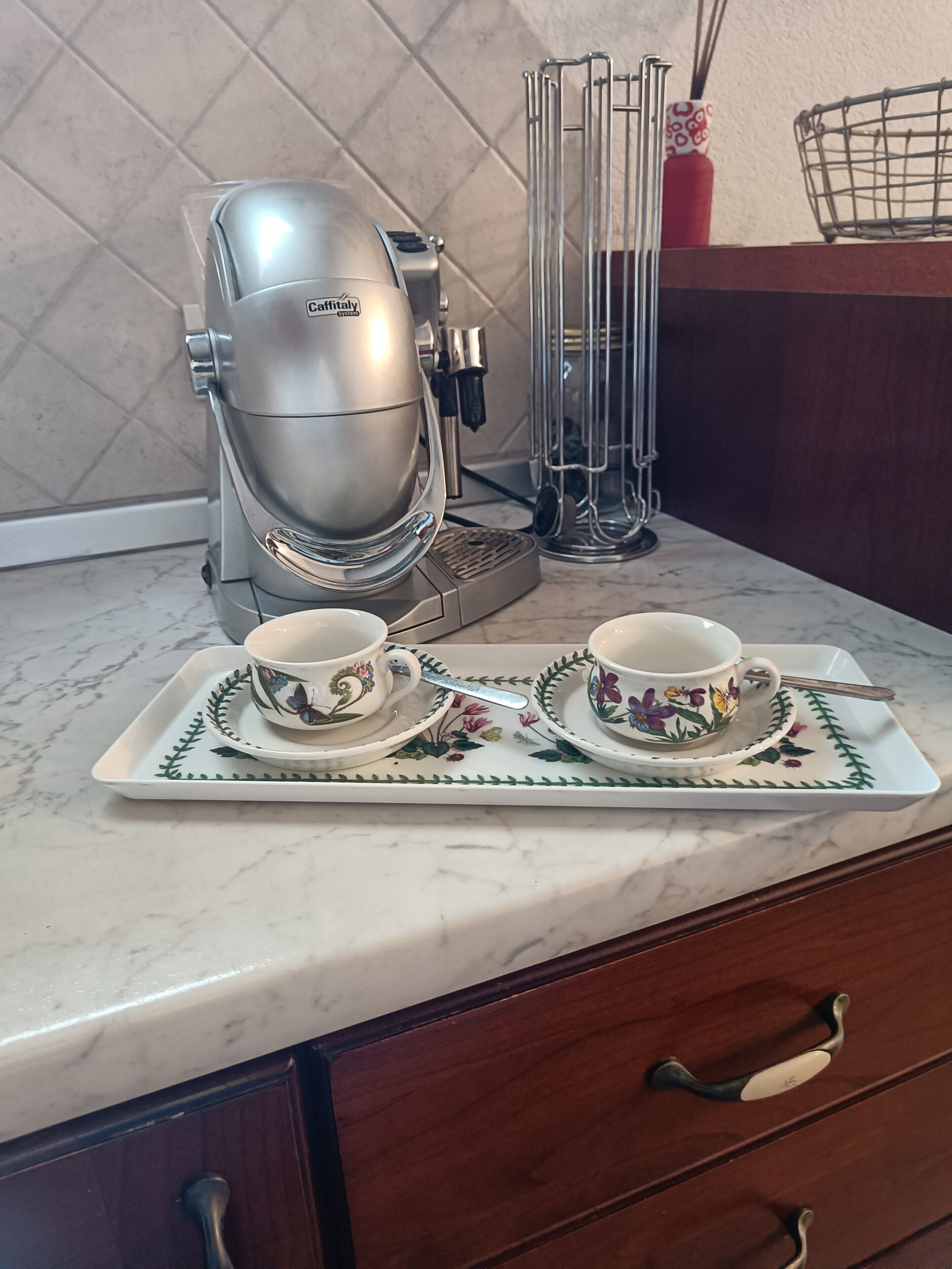 Eine Küchenarbeitsplatte mit Kaffeemaschine, zwei Tassen auf Untertassen, einer Ablage und einer Schublade mit Griffen.