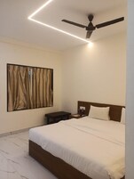 Un dormitorio con cama, mesita de noche, ventilador de techo y ventana con cortinas.
