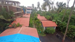 A residential area with multiple houses, some with red roofs, surrounded by lush greenery and palm trees. - Seashell Retreat (Shrivardhan)
