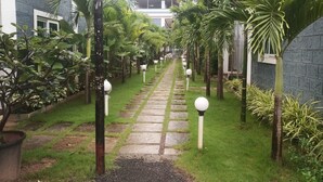 A pathway flanked by palm trees and potted plants, leading to a building with a modern design.