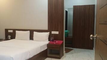 Een hotelkamer met een bed, nachtkastje, houten garderobe en een zichtbare badkamer door een open deur.