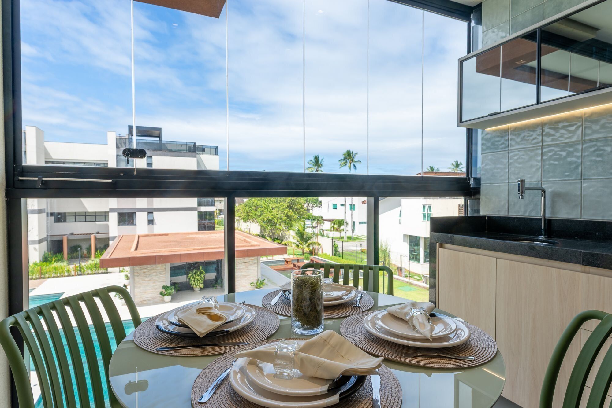 A dining area with a table set for four, overlooking a residential area with buildings and a clear sky.
