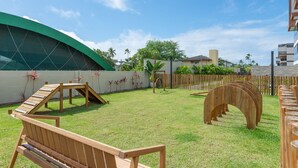 Un espacio al aire libre con césped, una estructura de juego de madera, un banco y un arco de madera curvo peculiar.