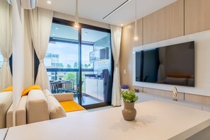 Un salon moderne comprenant un canapé, une table basse, un téléviseur à écran plat fixé au mur et une porte-fenêtre coulissante donnant sur un balcon.