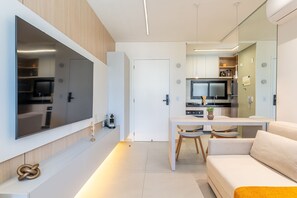 Un espace de vie moderne comprenant un téléviseur à écran plat fixé au mur, un canapé, une table à manger avec des chaises, et un coin cuisine équipé d’un four à micro-ondes et d’une cuisinière.