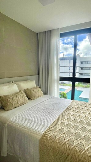Ein Hotelzimmer mit einem großen Bett, Blick auf einen Swimmingpool und einem modernen Gebäude im Hintergrund.