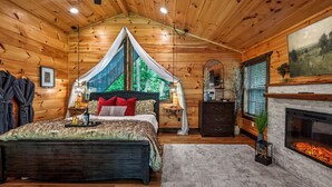 A log cabin bedroom with a bed, a fireplace, and a large window. - Romantic Luxury Cabin • Hot Tub • Fire Table • EV (Sevierville)