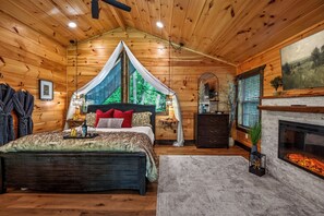 Quarto de cabana de toras com uma cama, lareira e uma janela grande.