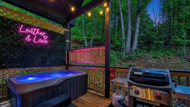 A hot tub and grill on a wooden deck with a neon sign reading 'Leather & Lace'. - Romantic Luxury Cabin • Hot Tub • Fire Table • EV (Sevierville)