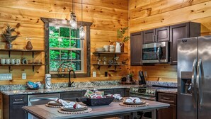 A wooden cabin interior with a kitchen area, including a refrigerator, microwave, and wooden cabinets. - Romantic Luxury Cabin • Hot Tub • Fire Table • EV (Sevierville)