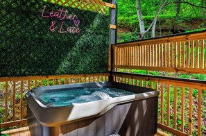 A hot tub with a wooden deck and a green hedge backdrop. - Romantic Luxury Cabin • Hot Tub • Fire Table • EV (Sevierville)