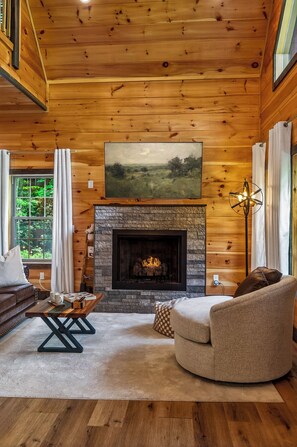 A cozy cabin interior with a stone fireplace, wooden walls, and a comfortable seating area. - Romantic Luxury Cabin • Hot Tub • Fire Table • EV (Sevierville)