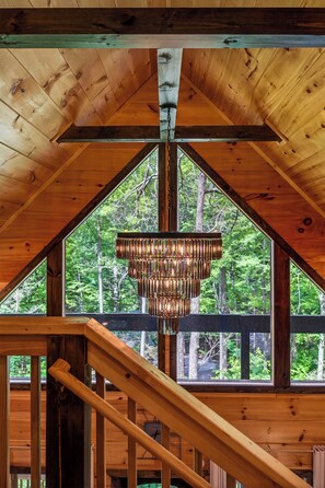 A wooden interior with a large window and a hanging light fixture. - Romantic Luxury Cabin • Hot Tub • Fire Table • EV (Sevierville)