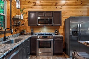 A modern kitchen with stainless steel appliances, wooden cabinetry, and granite countertops. - Romantic Luxury Cabin • Hot Tub • Fire Table • EV (Sevierville)