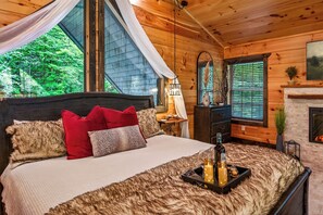 Une chambre confortable avec un grand lit, une cheminée et une vue sur la verdure environnante.