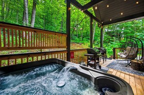 Un bain à remous avec une terrasse en bois et des meubles d’extérieur, le tout entouré d’une forêt.
