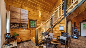 A wooden interior with a staircase, seating area, and a fireplace. - Romantic Luxury Cabin • Hot Tub • Fire Table • EV (Sevierville)