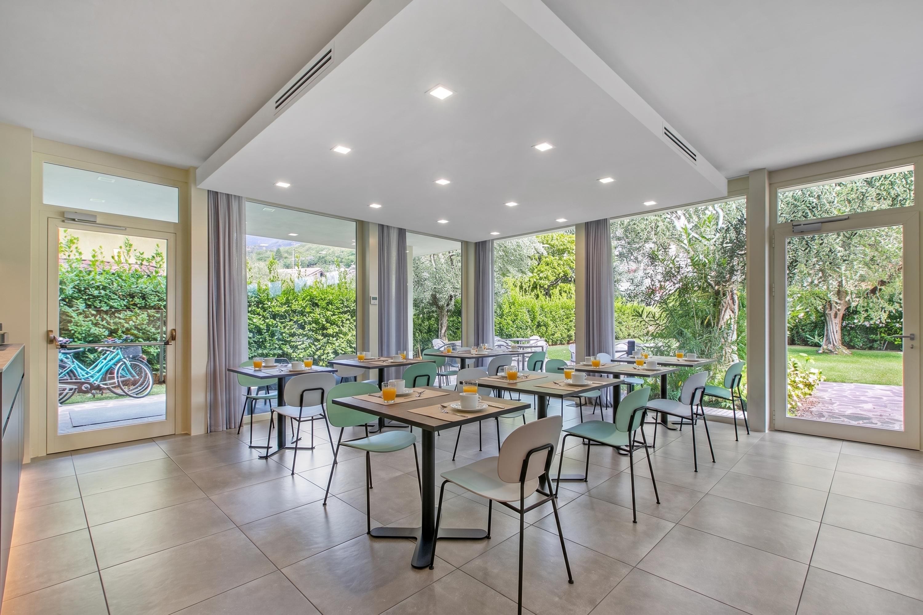 Un espace de restauration moderne, doté de plusieurs tables et chaises, de grandes fenêtres offrant une vue sur la verdure et d’un plafond pourvu d’un éclairage encastré.