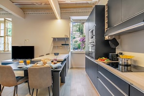 A modern kitchen with a dining area, featuring a flat-screen TV, breakfast setup, and a view of the outdoors. - Boutique Apartment (Toscolano Maderno)