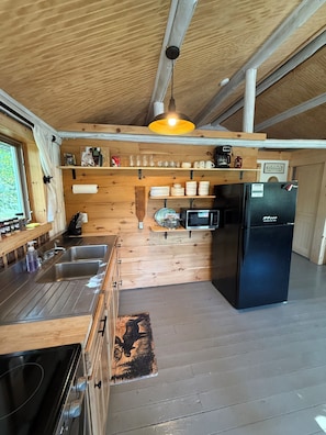 A compact kitchen with wooden cabinetry, a black refrigerator, and a wooden ceiling.