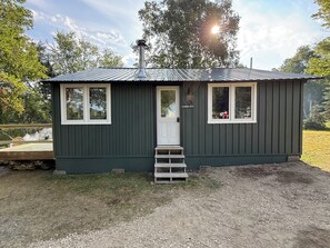 A small, single-story cabin with a metal roof, a front door, and a small porch with steps.