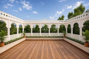 Un vaste espace extérieur doté d’un plancher en bois, de murs recouverts de treillis blancs et de plantes en pot.