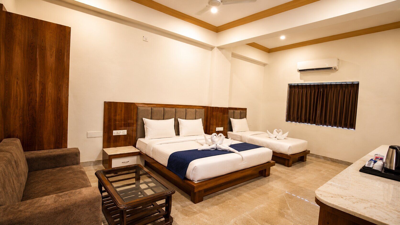 A hotel room with a large bed, a sofa, a small table, and a window with curtains.