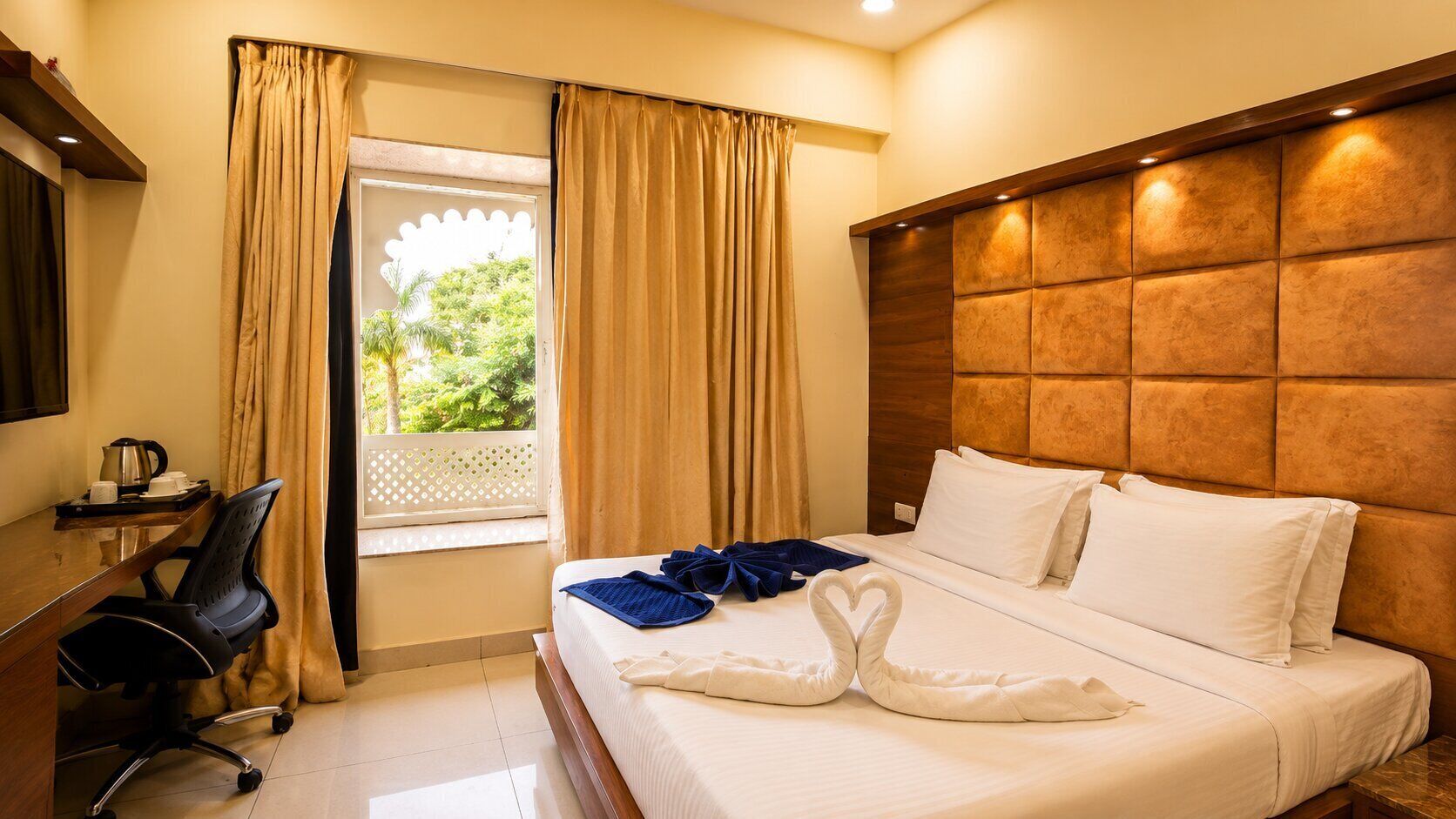 Una habitación de hotel con cama, escritorio, silla y ventana con cortinas.