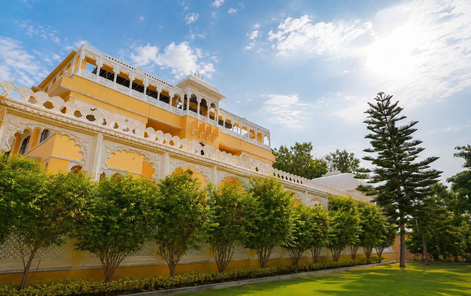 A traditional building with ornate white balconies and a yellow facade, surrounded by lush greenery.