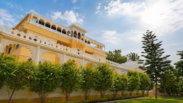 A traditional building with ornate white balconies and a yellow facade, surrounded by lush greenery.
