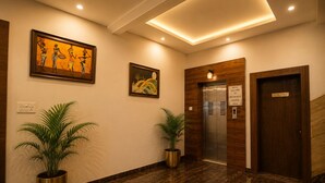 Un vestíbulo de hotel con piso de mármol, dos plantas en macetas, un cuadro, un ascensor y una puerta con la leyenda 'NO ENTRY'.