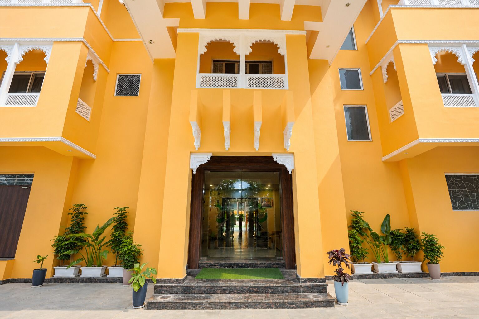 A building with a central entrance, multiple balconies, and potted plants.