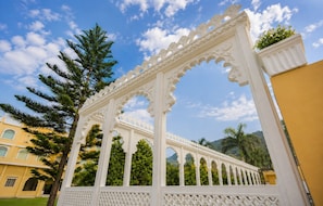 Une structure blanche et richement décorée, ornée de sculptures complexes, entourée de verdure et surplombée par un ciel dégagé.