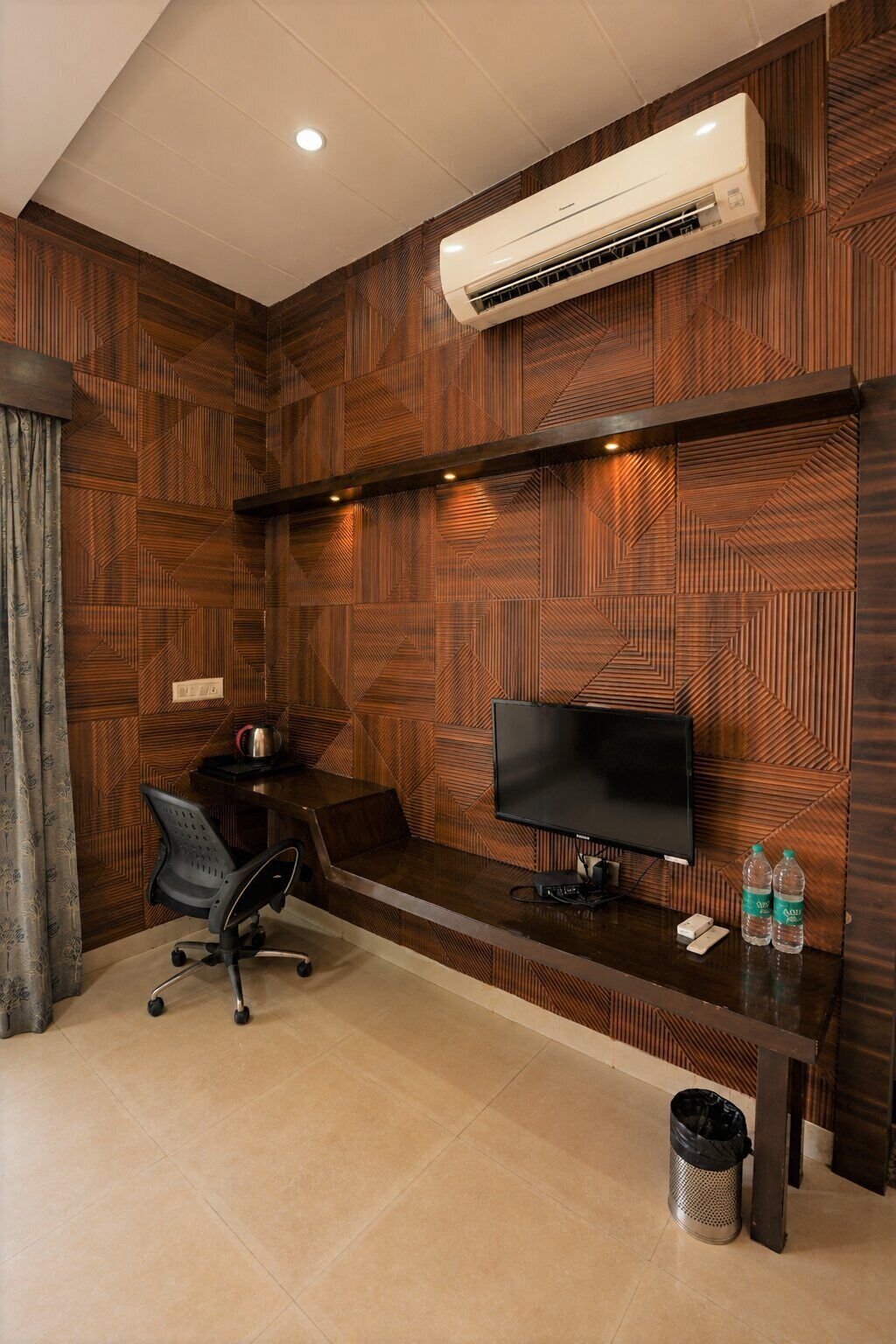 A modern room with a wooden wall panel design, a flat-screen TV, a desk with a chair, and an air conditioning unit mounted on the wall.