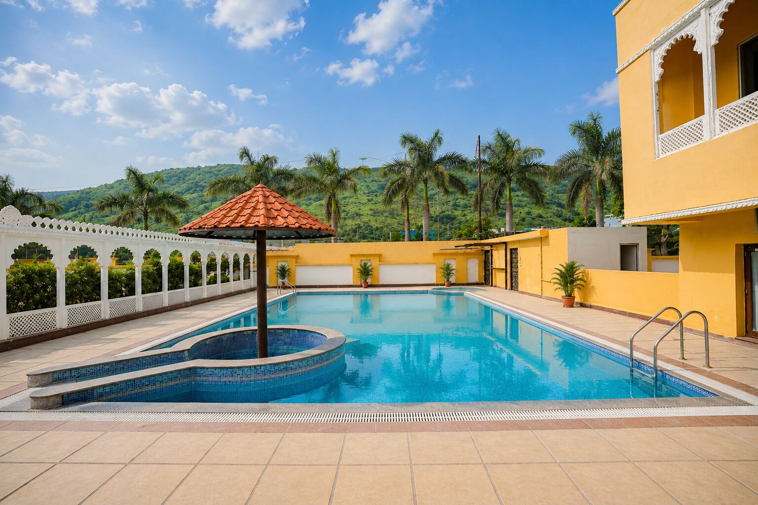 A swimming pool with a tiled deck, surrounded by a white fence and palm trees, with a mountain in the background.