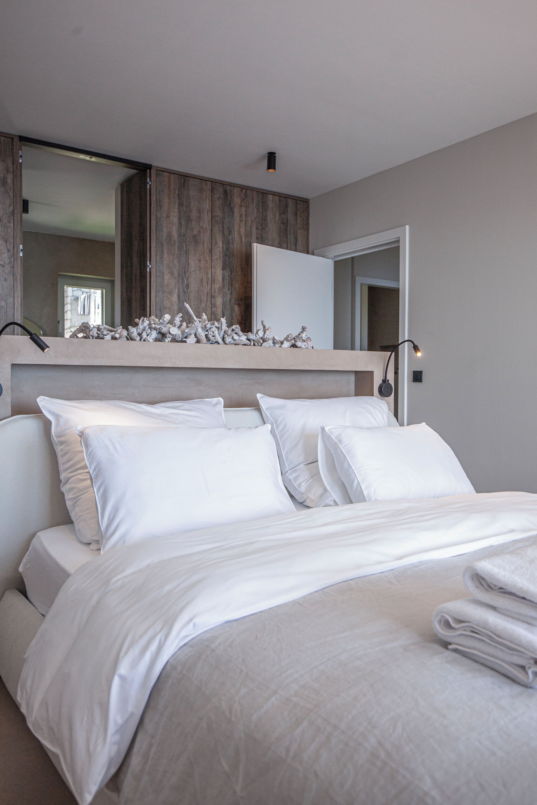 A modern bedroom with a large bed, a wooden headboard, a mirror, and a wall-mounted light fixture.
