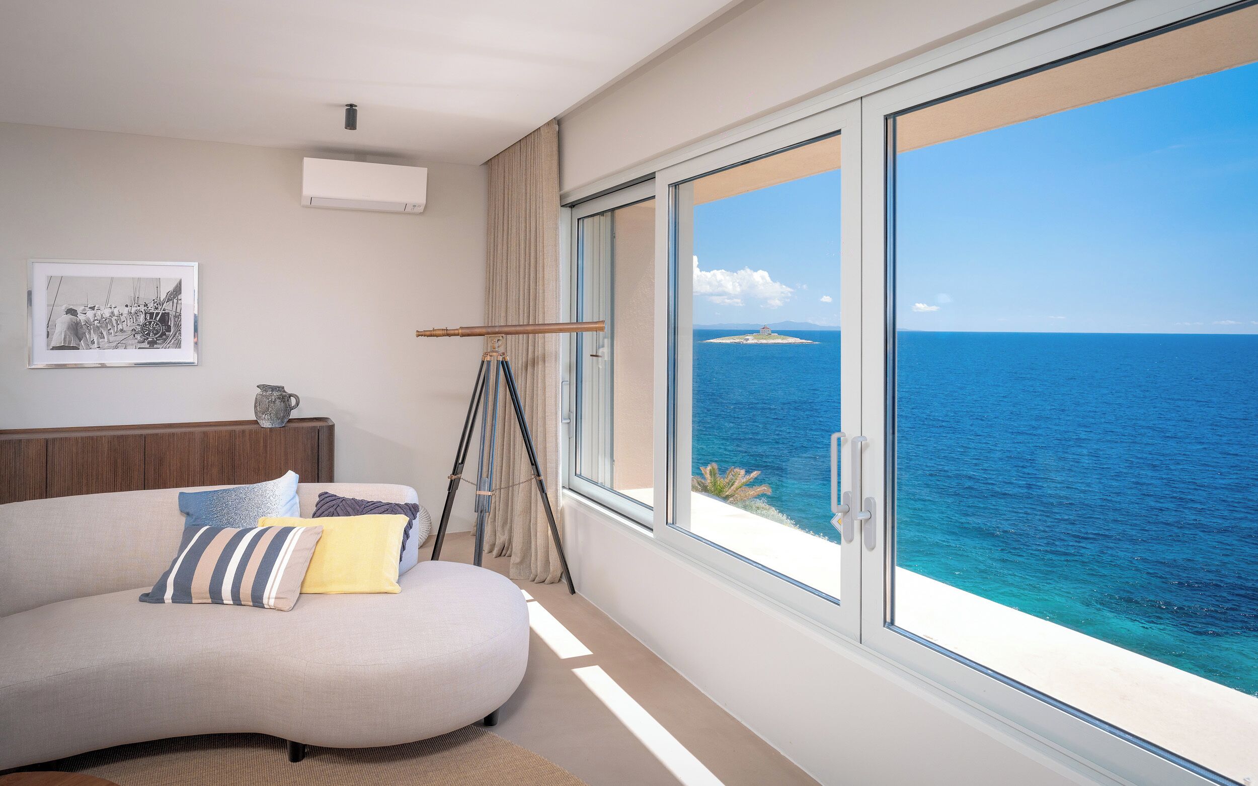 A modern room with a curved sofa, a telescope, and a large window overlooking the sea.