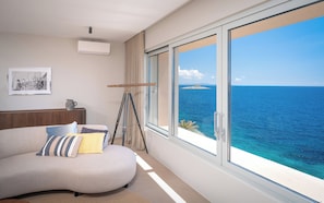 A modern room with a curved sofa, a telescope, and a large window overlooking the sea. - Beachfront Villa Atropos (Hvar)